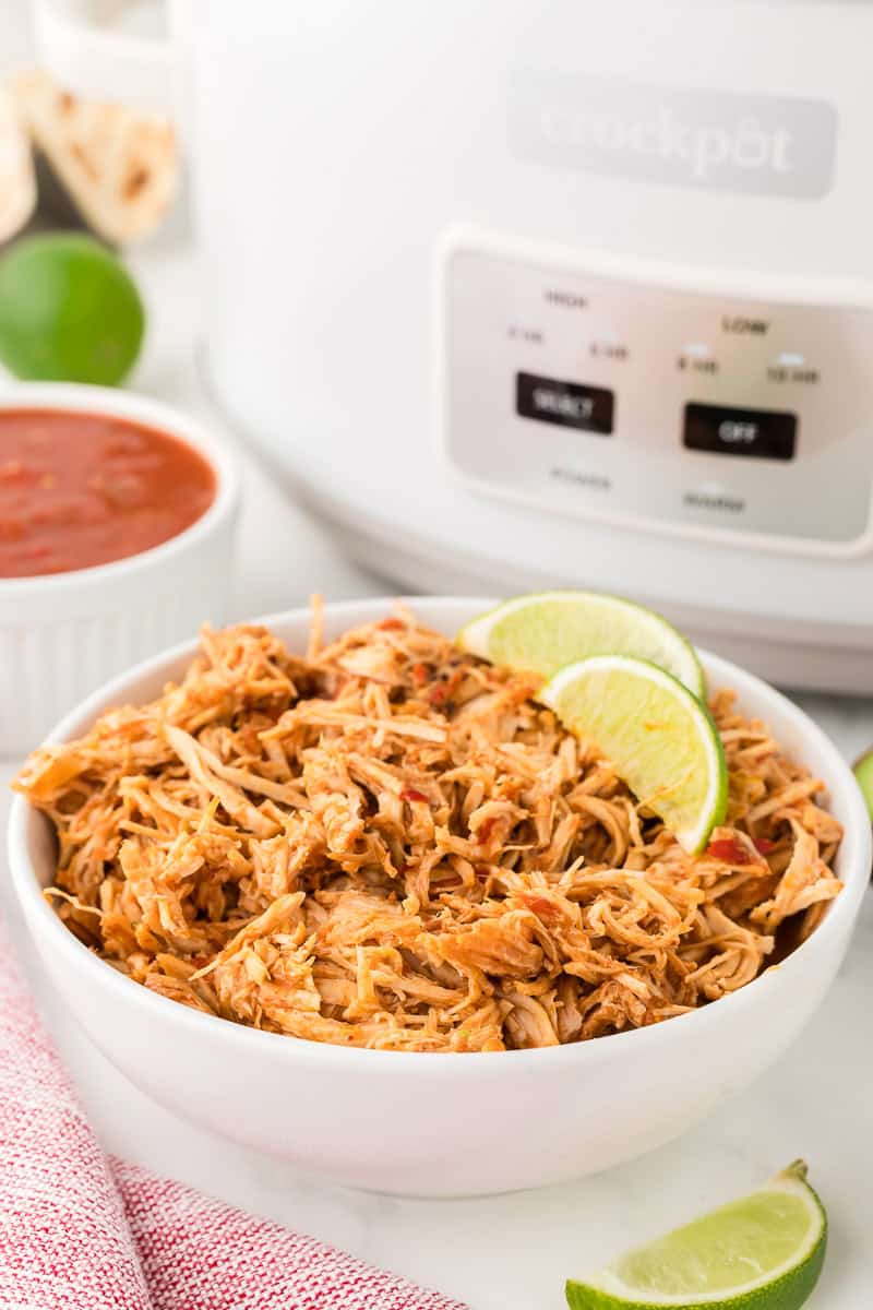 slow cooker salsa chicken in a bowl in front of a crock pot