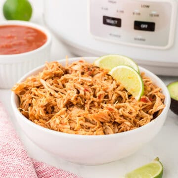 slow cooker salsa chicken in a bowl in front of a crock pot